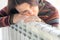 Woman wearing pullover sitting near heater radiator and hugs it