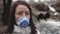 Woman wearing a real anti-pollution, chemical discharge into a river and viruses face mask. Dirty sewage from the pipe