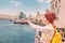 Woman wearing a red turban and carrying a yellow backpack pointing to a passing cruise ship in the old Dubai Creek