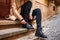 Woman wearing trench coat sitting on stairs and tying shoelace on her black boot