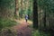 Woman wearing warm winter coat walking alone along a winding path through a dense woodland.