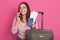 Woman wearing in white casual shirt with red stripes with travel suitcase and passport, standing and speaking via smartphone,