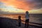 Woman wearing white jacket and little child are walking on Baltic Sea coast on sunset of winter day. Outdoors activity for family