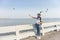 Woman wearing white shirt, wearing hat and carrying bag, raising her arms to feed the seagull, Bang Pu, Thailand