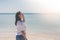 Woman wearing white t-shirt, she standing on sand beach and holding sunglasses in hand with beautiful seascape view.
