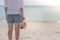 Woman wearing white t-shirt, she standing on sand beach and holding weave hat in hand, she looking at the sea.