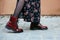 Woman wears dark red ankle boots, dark stockings and a flowered long dress, photographed to the knee