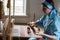 The woman is weaving the colorful cotton robe or dress by using wooden loom in the local village in Russia