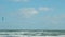 A woman in a wetsuit on a parachute rides a board on the waves of the sea. A young man performs a trick in the air