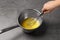 Woman whipping melting butter in saucepan on grey table