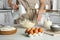 Woman whipping white cream with mixer at light grey table in kitchen, closeup