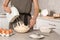 Woman whipping white cream with mixer at light grey table in kitchen, closeup