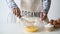 Woman whisks chicken eggs lying in a glass bowl with a kitchen whisk