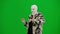 Woman in white balaclava, fur coat and dress walking and dancing merrily with her hands up. Woman freak on green