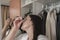 Woman in a white bathrobe applying eye drops with a small bottle in front of the mirror on the closet door in her bedroom