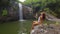 Woman in white bikini looking at the waterfall in jungles. Hiker girl trekking, enjoying beautiful waterfall. Ecotourism