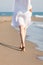 Woman in white cotton dress walking on sandy beach sunny summer day lower body back