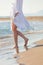 Woman in white cotton dress walking on sandy beach sunny summer day lower body side