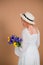 A woman in a white dress and hat stands with her back and holds a bouquet of tulips and irises. March 8. Women\'s Day. Women\'s holi