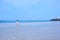 Woman in white dress with her long hair blowing in the wind, walking in a beach with white lighthouse on rocky platform in Jeju Is