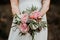 Woman in white dress holds a green  white and pink flower bouquet.