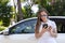 a woman in a white dress near an expensive car writes an SMS to the phone, calls the help service or writes to friends