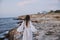 Woman in white dress walks on the beach stones back view