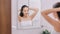 Woman in white dressing gown tying up her hair in front of mirror in photo of bright bathroom