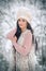 Woman with white fur cap and sheepskin smiling enjoying the winter scenery in forest. Side view of happy brunette girl posing