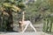 A woman in a white gymnastic jumpsuit is engaged in yoga on the background of water and a green mountain slope