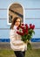 A woman in a white jacket with a bouquet of red roses in front of a house.