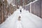 A woman in a white jacket and a dog walk in the snow after a winter storm in a snowy forest. Active dog walking on the street on a