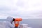 Woman in white jacket and hood looks in binoculars at sea waterfront with sea view. Side view.