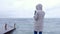 Woman in a white jacket takes a mobile phone storm waves standing on embankment. Back view.