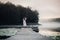 Woman in white light dress run on the pier on foggy morning lake.
