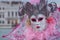 Woman in white mask and decorative pink feathers and jester`s costume at Venice Carnival