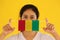 A woman in white shirt with Guinea flag on hygienic mask in her hand and lifted up the front face on yellow background. Tiny