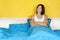 Woman in white shirt sitting alone on double bed