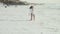 A woman in a white shirt walks along the shore of ocean