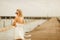 Woman in white short wedding dress. bride in glasses with blond hair standing at the pier.