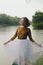 Woman in white skirt, yellow sweater near river in rainfall