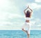 Woman in white sportswear doing yoga on a wooden pier. Sea and