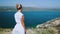 Woman in white summer dress admiring from the top scenic mediterranean landscape. Dress flying in the wind. Amazing