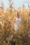 Woman in a white summer long dress walks on a cornfield and posing in sunset time