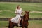 A woman in a white sundress riding a horse in a field