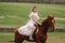 A woman in a white sundress riding a horse in a field