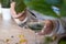 a woman in a white sweater adds drops of chlorophyll to a glass of water standing next to palm trees