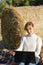 Woman in a white sweater on the background of a haystack with a laptop in her hands sits on the ground