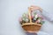 A woman in a white sweater holds a wicker basket with flowers on a white background, close-up without a face. Congratulations conc