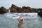 Woman in white swimsuit enjoys relaxation in sea. Female unwinds in ocean waters, natural rocky coast background